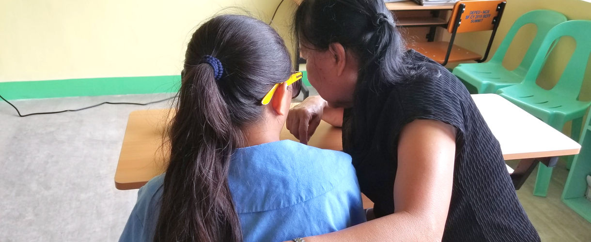 A woman and girl sitting close and talking in a classroom.
