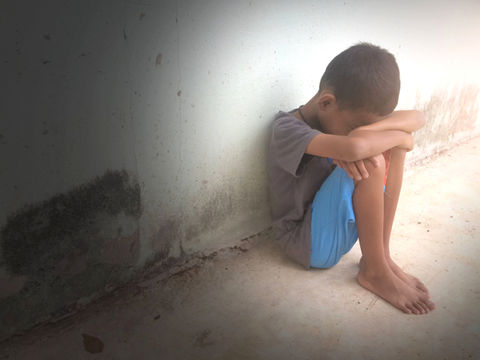 Child sitting on the ground with his head on his knees.