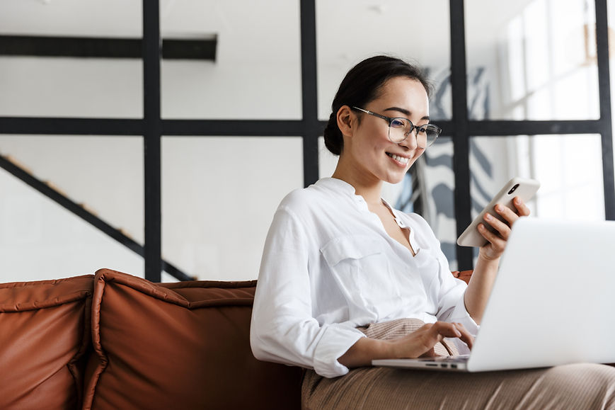Attractive smiling young asian business woman relaxing on a leather couch at home, working