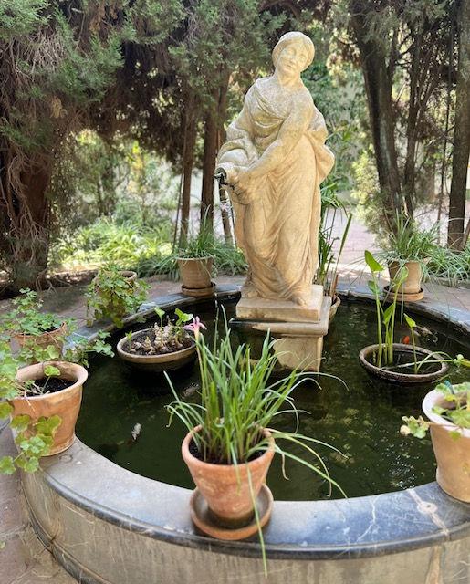 lady figure fountain garden feature surrounded by trees and plants