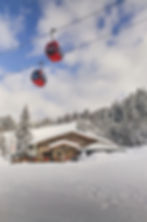 Zwei rote Gondeln über verschneiter Berghütte mit Tannenbäumen im Winter.