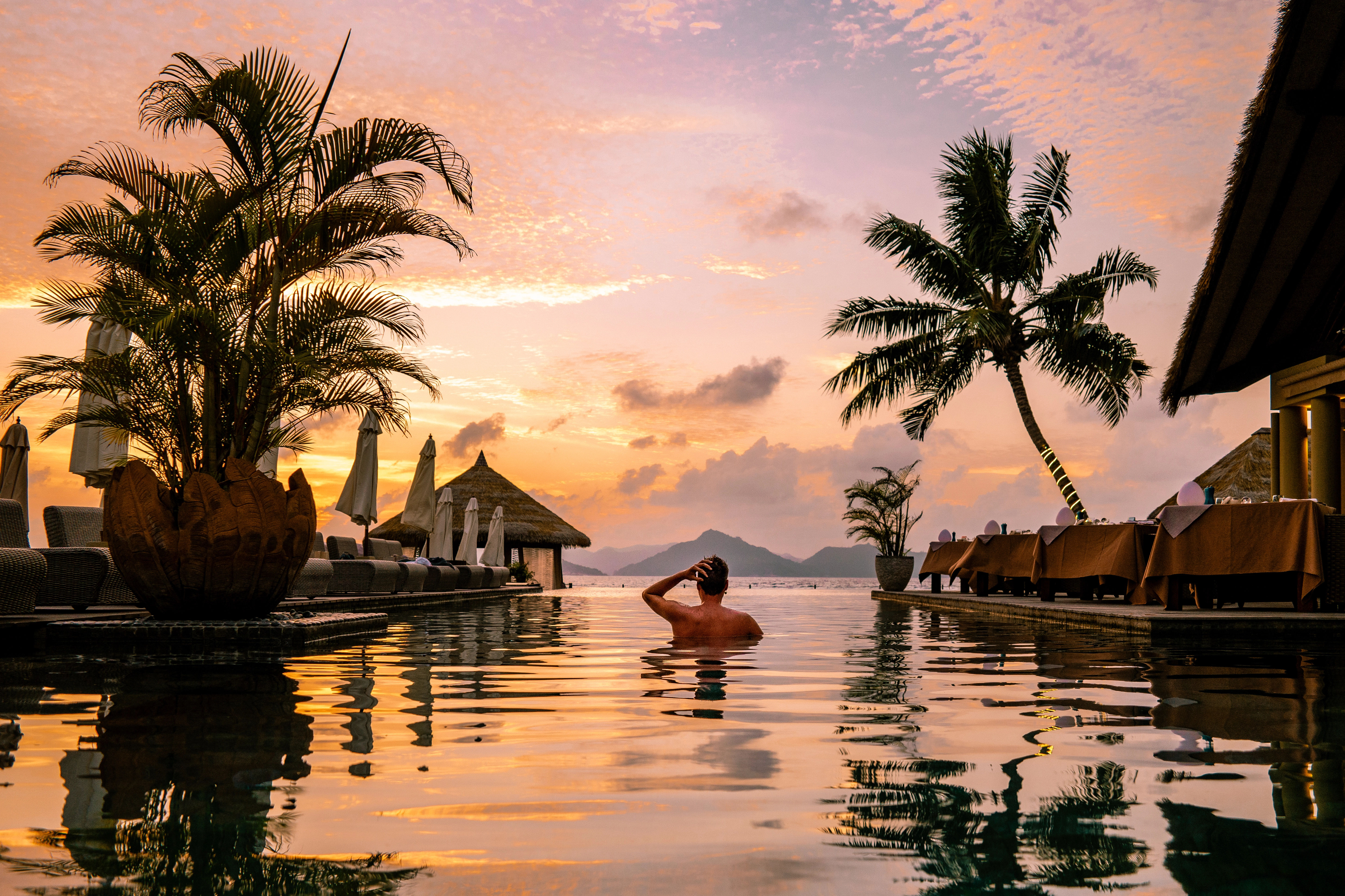 Young men in swimming pool during sunset, Luxury resort Seychelles
