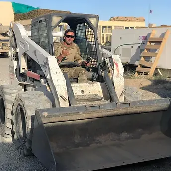 Owner operating a skid steer loader on a construction site, performing land clearing and grading for excavation and site preparation in North Carolina