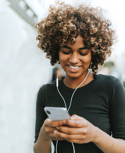 Image of a woman of color working on her cell phone and wear ear phones.