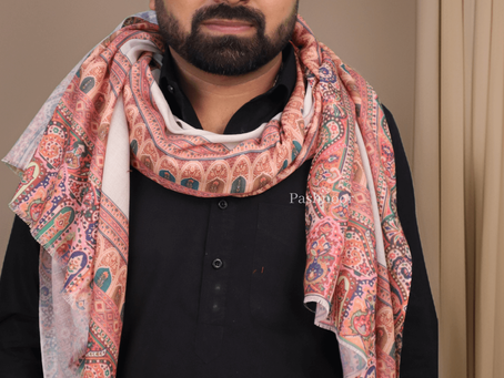 The image showcases a confident man elegantly styled in a luxurious Pashnoor shawl. The shawl features intricate, multicolored traditional Kashmiri patterns in warm hues of peach, maroon, green, and ivory. Draped gracefully over a classic black kurta, the shawl adds a vibrant and regal touch to the ensemble. The backdrop is minimal, allowing the artistry of the fabric and the brand’s elegance to shine. The logo and name “PASHNOOR” are subtly placed in the top right and bottom center, reinforcing the brand’s identity.