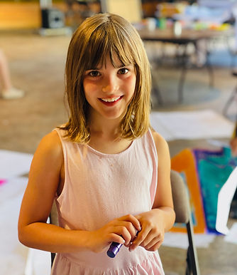 Child smiling while participating in an art activity during Mr. D's Music Club summer camp.