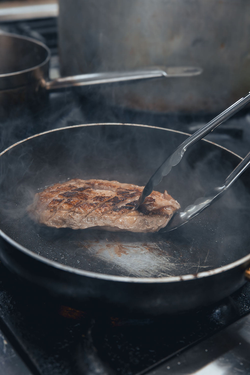 Fleisch brät in heißer Pfanne mit Zange.