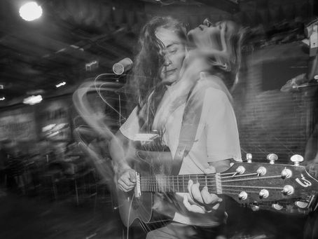 A girl playing the guitar that has a light drag making her look like shes throwing back her head.