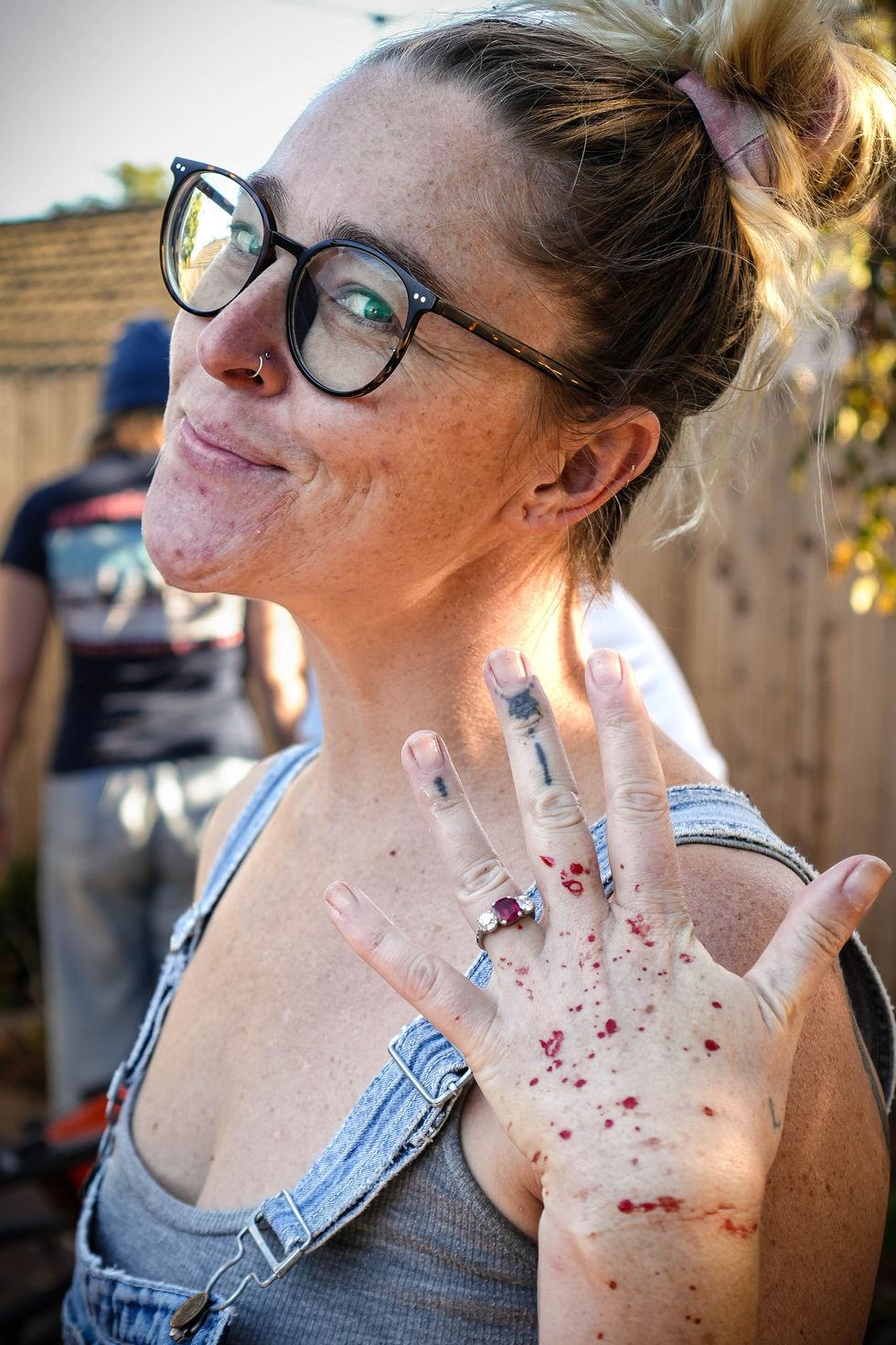 A woman raises a blood-splattered hand proudly, smiling as her ruby engagement ring gleams.
