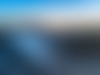 Aerial view of misty mountains at sunrise, with a blue and orange sky. Clouds blanket the valley, creating a serene and dreamy atmosphere.