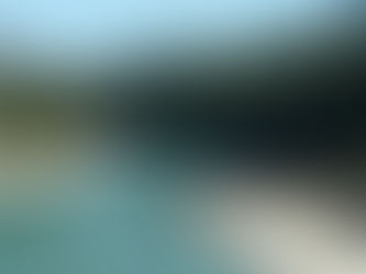 River winding through forested mountains under a clear blue sky. Rocks line the shore, with a small inflatable boat visible. Peaceful scene.