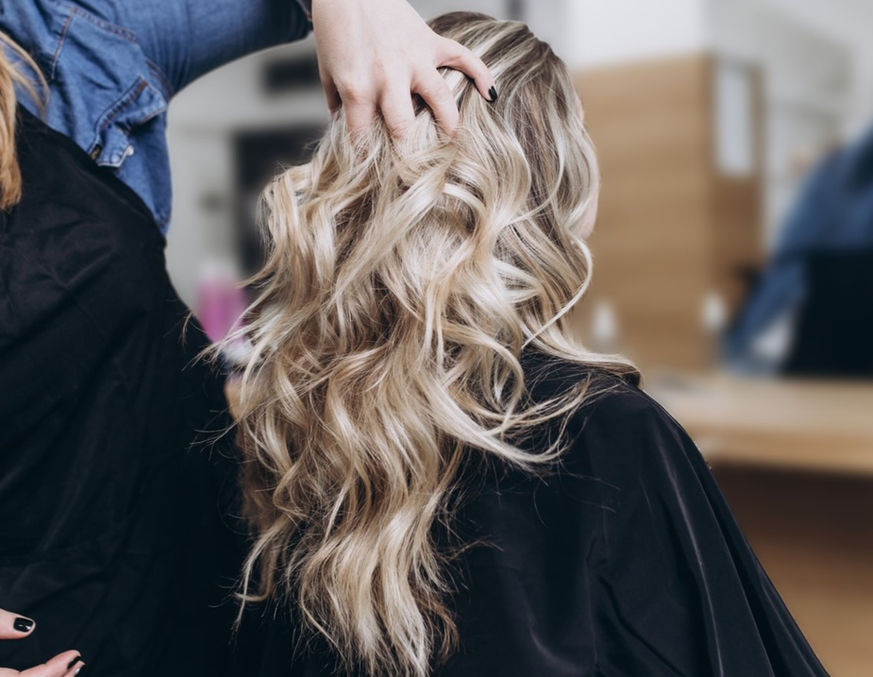 image of a women with blonde, long curly hair sitting in a chair at Hidden gem salon and spa while a highly experienced hairstylist and expert colorist styles her hair