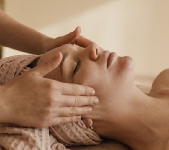 image of a women looking very happy and relaxed, laying on a spa table with a towel on her head with golden lighting while by the excellent hair salon Hidden Gem's highly experienced expert esthetician