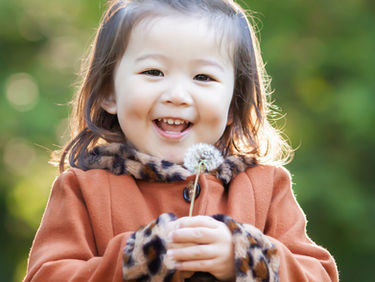 A young girl holding a dandelion in a park on an autumn day