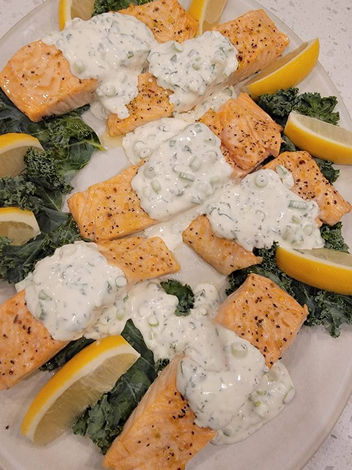 Picture of a luxurious salmon dinner topped with a creamy sauce, lemon and asparagus. 
