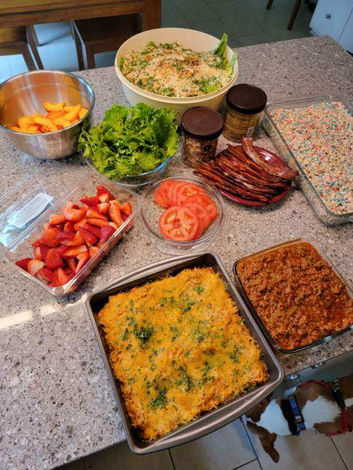 Photo of an arragement of food that was prepared for dinner. Food items included are a dinner bake, tomatoes, strawberries, lettuce, bacon, dessert and salad. 