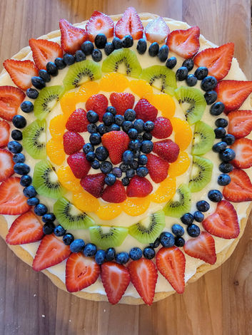Picture of a fruit pizza containing strawberries, blueberries, kiwi, oranges and raspberries on top of a cookie crust. 
