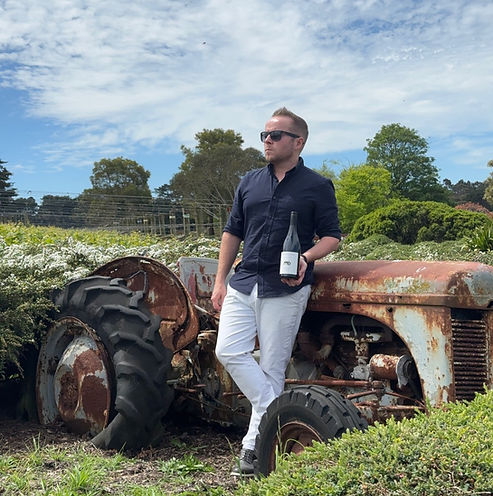 Paul Laurie leaning against a tractor in a vineyard with a bottle of wine