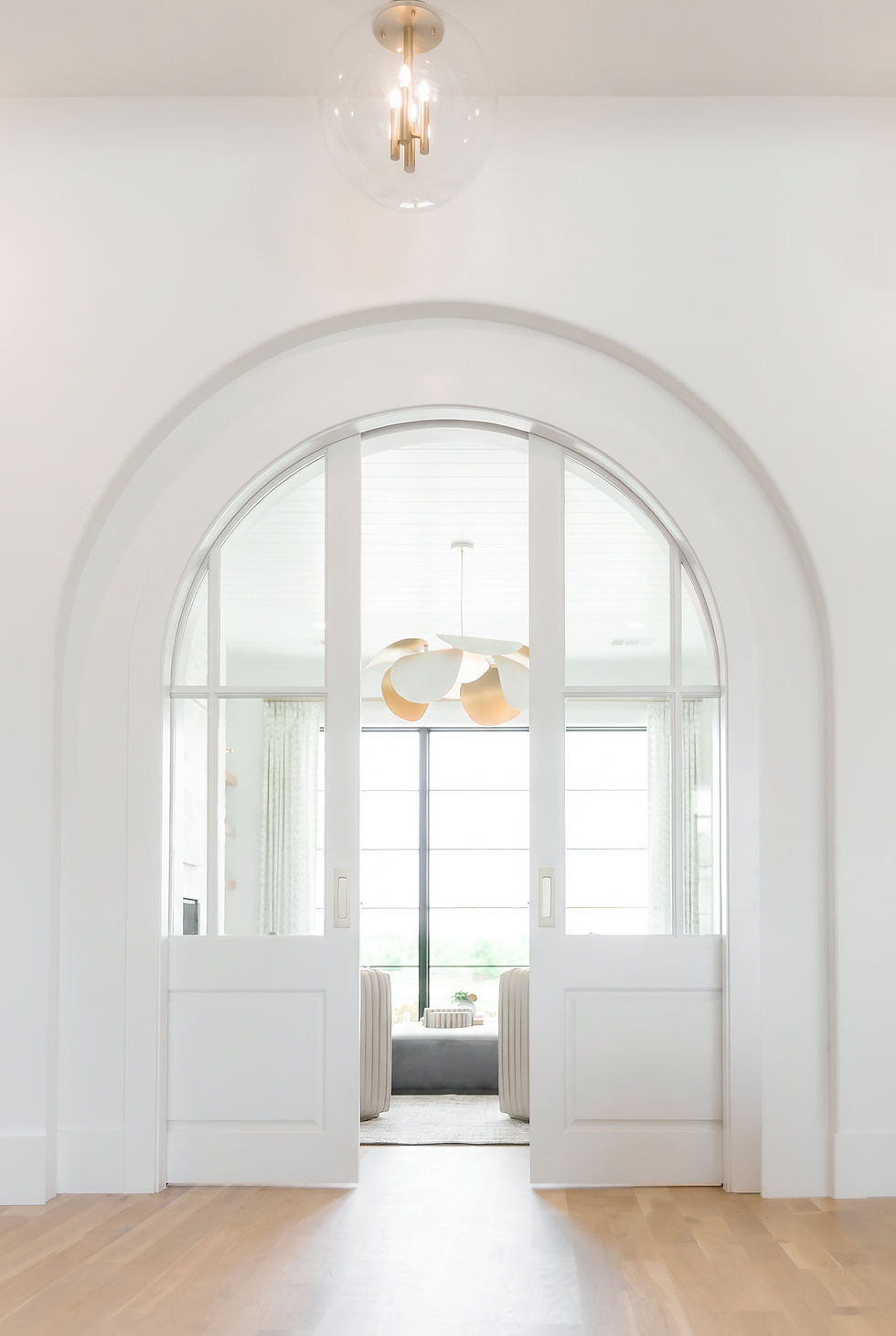 Bright luxury interior with a dramatic arched doorway, custom glass-paneled sliding doors, light oak flooring, and a softly f