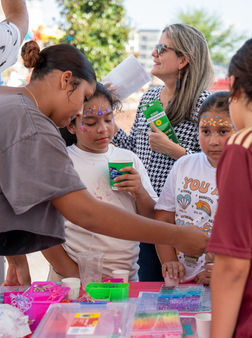 Two children with their faces decorated with paint are at an arts and craft booth at a community charity event.
