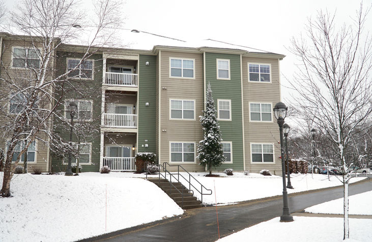 Winter view of a multi-unit residential building with a cleared sidewalk after snowfall