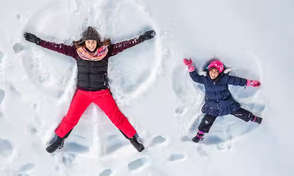 Girl and child lying in the snow making snow angels during winter.