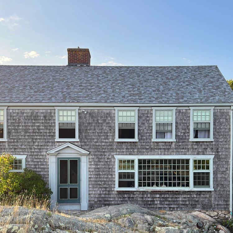 New England 2 story home with long grasses blowing in the wind in front