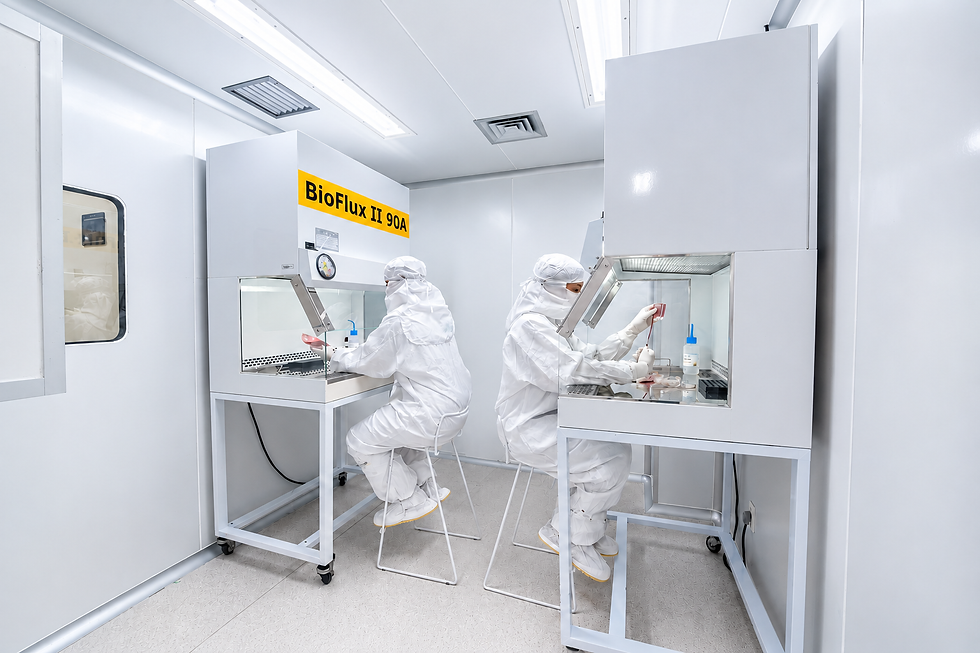 Laboratório de biotecnologia com dois profissionais paramentados realizando procedimentos em cabines de segurança biológica, com equipamentos e iluminação controlada para o processamento de amostras celulares.