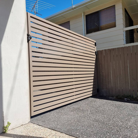 Closed wooden gate with horizontal slats, driveway, and house behind. custom metal fabrication service