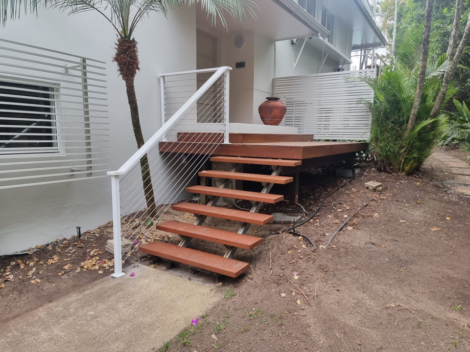 Wooden steps and white railing leading to a deck near green plants