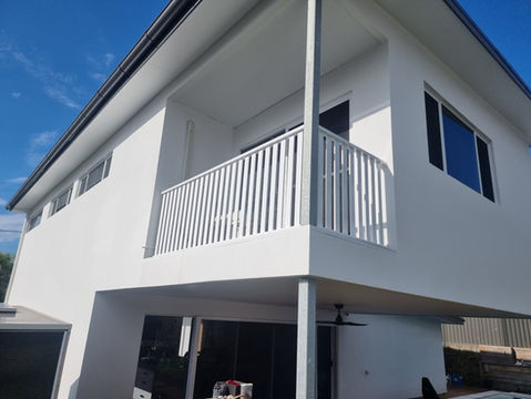 White modern building with balcony, railing, and windows under clear blue sky.