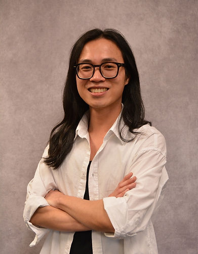 Smiling person with glasses and long hair crossing arms