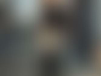 Man holding grocery bags stands on urban sidewalk, wearing a jacket and ripped jeans. Background shows buildings and a bus stop. Mood is somber. SNAP freeze