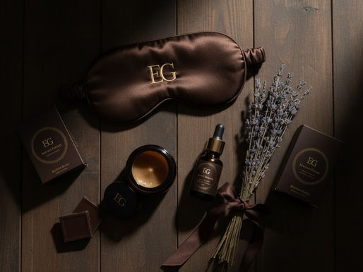 Brown sleep mask, cream, dropper bottle, and lavender bundle on wooden surface. Items have EG branding. Mood is calm and luxurious. Self-care Sundays