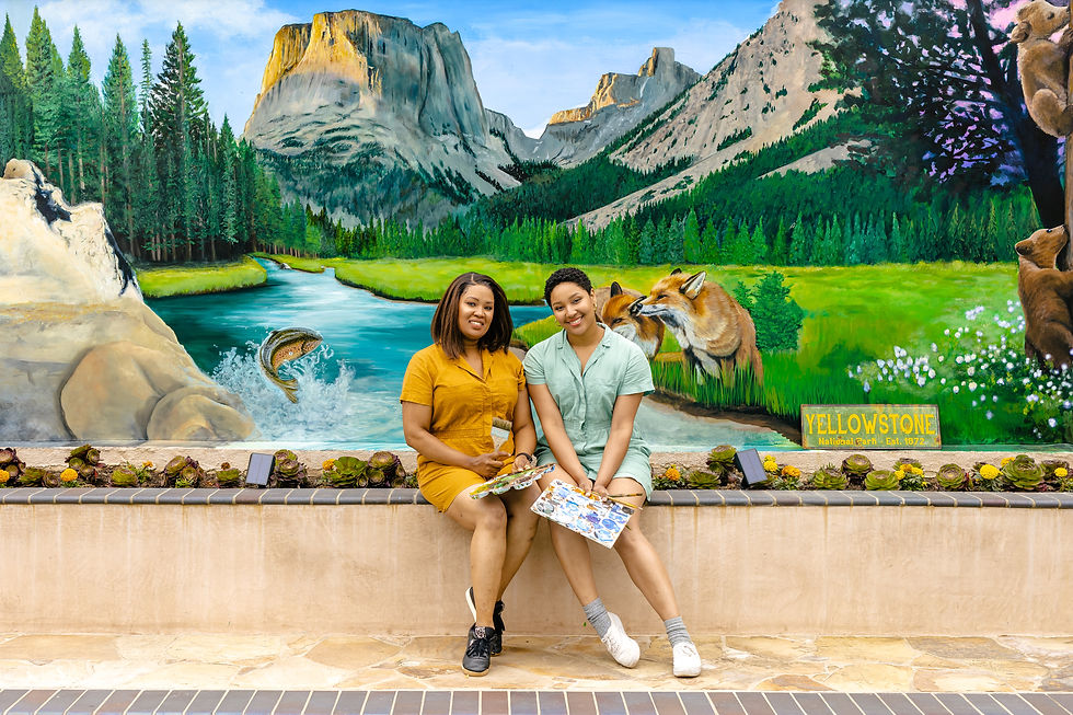 Two artists sitting in front of their mural holding paint palettes.
