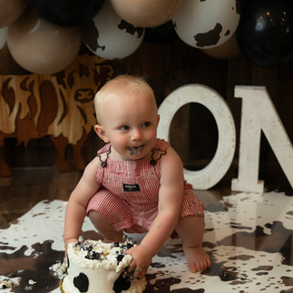 Baby in suspenders and cowboy hat during cake smash in Apple Valley