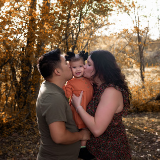 mom and dad kissing little girl for fall photo