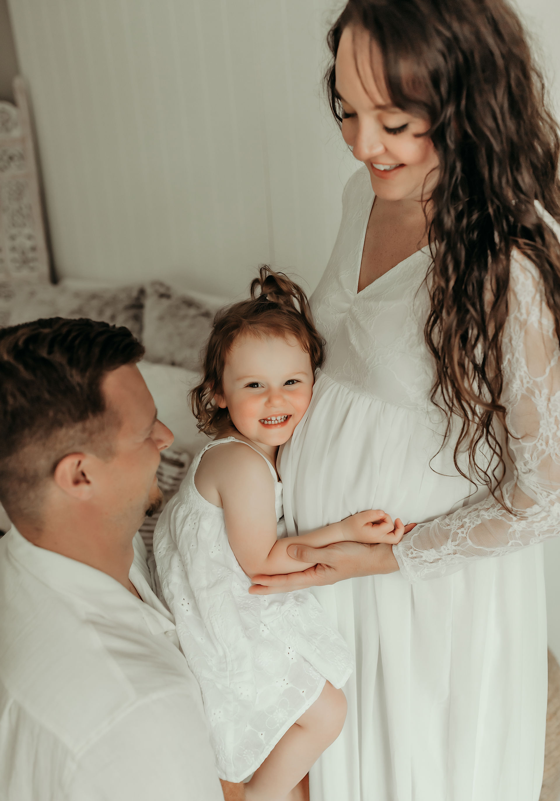 Expecting parents looking down at their daughter during an intimate family maternity photoshoot.