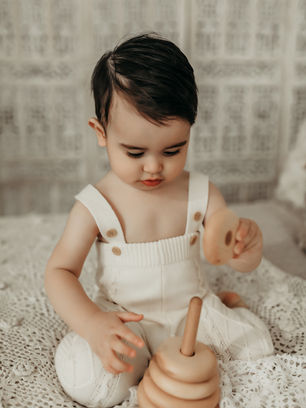 Minimalist milestone portrait of toddler boy in white overalls, photographed in a luxury Minneapolis baby photography studio with timeless neutral styling by Elsiebel Photography.