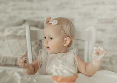 Baby girl looking curiously at her cupcake with frosting-covered hands. Luxury cake smash photography by Elsiebel Photography, Minneapolis metro.