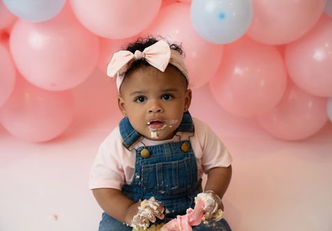 First birthday cake smash session in Burnsville, MN with a “Mrs. Rachel” theme featuring a baby girl in denim overalls and pastel balloon décor, Elsiebel Photography serving Eden Prairie, Apple Valley, and Edina families.