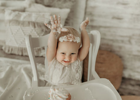 Baby giggling with arms raised, surrounded by frosting and joy. Luxury first birthday cake smash photo by Elsiebel Photography, Minneapolis metro.