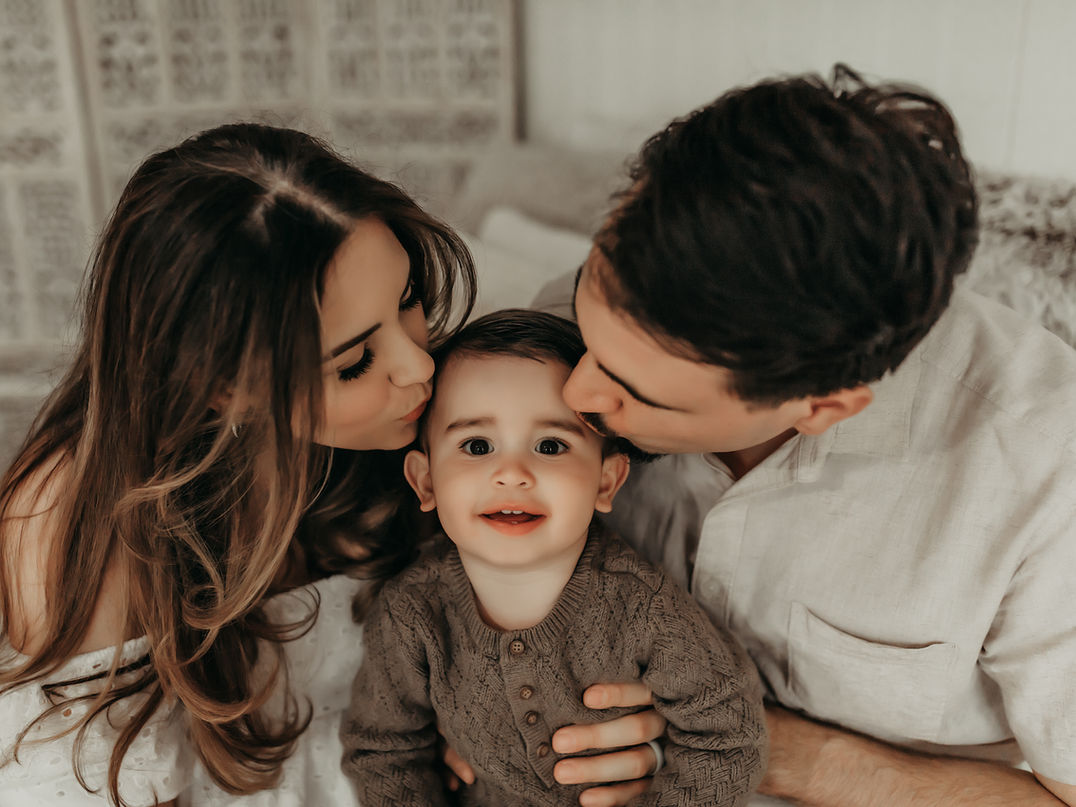 Luxury milestone family portrait of parents kissing toddler boy in a soft neutral Minneapolis photography studio by Elsiebel Photography, capturing timeless family connection and milestone memories for Twin Cities families.