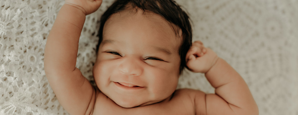 Smiling newborn baby boy with hands raised during a cozy newborn session in Maple Grove at Elsiebel Photography