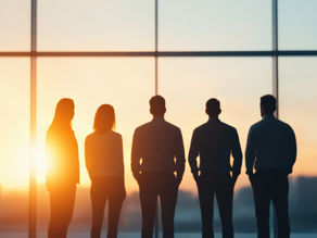 Business people silhouetted in office window looking at sunset city, representing leadership, success, and teamwork