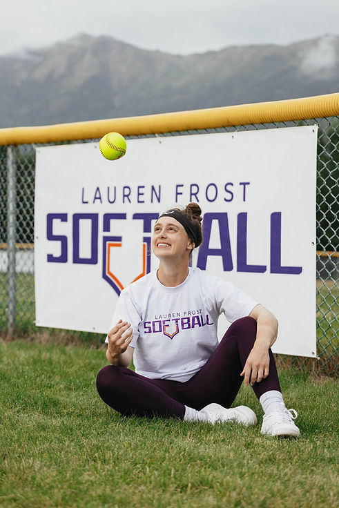Lauren Frost looking at a tossed ball while sitting in front of a Lauren Frost Softball banner.