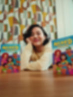 Sara Amini lounging on wooden floor with two copies of her graphic novel"Mixed Feelings"