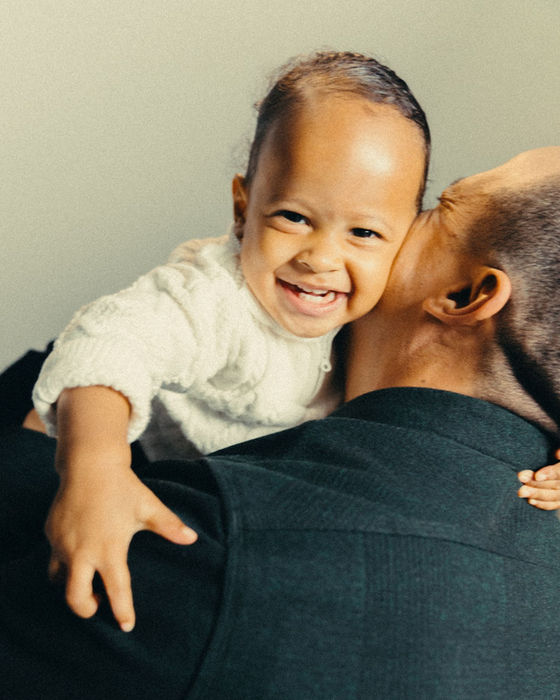 Adult kisses smiling baby on shoulder