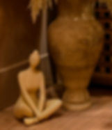 Sculpture of a woman sitting near a vase with dried flowers.