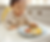 Child in polka dot shirt sits in high chair, focused on picking small fruit pieces from a gray plate in a bright kitchen setting.